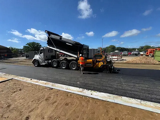 Dump truck feeding an asphalt paver on a new lot