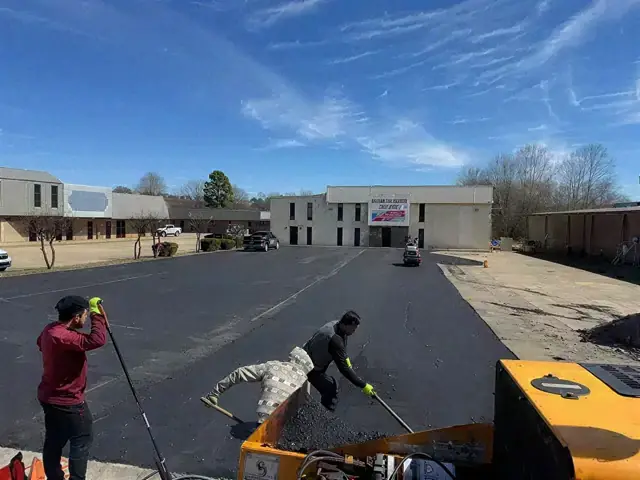 Two workers spreading hot asphalt with rakes on a parking lot