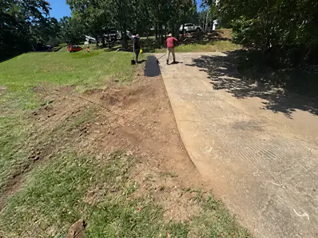 New asphalt driveway curving up a grassy slope toward a house