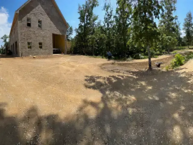 Gravel drive under construction next to a house being framed