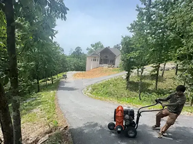 Worker running a walk-behind machine on a fresh asphalt drive