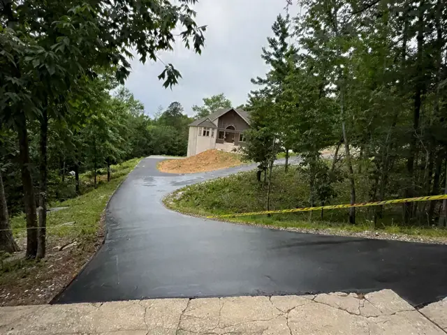 Freshly paved driveway curving toward a house through trees