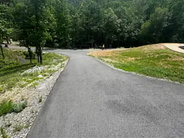 New asphalt driveway edge beside a lawn and trees